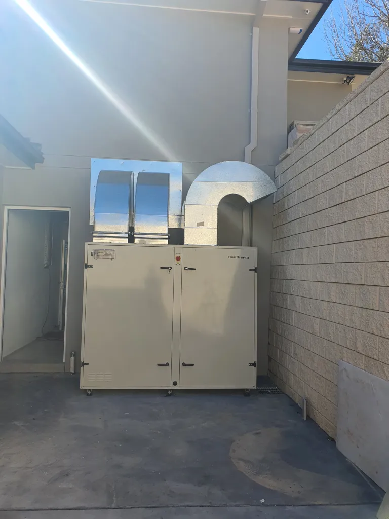 Outdoor pool dehumidification unit with ductwork beside a brick wall