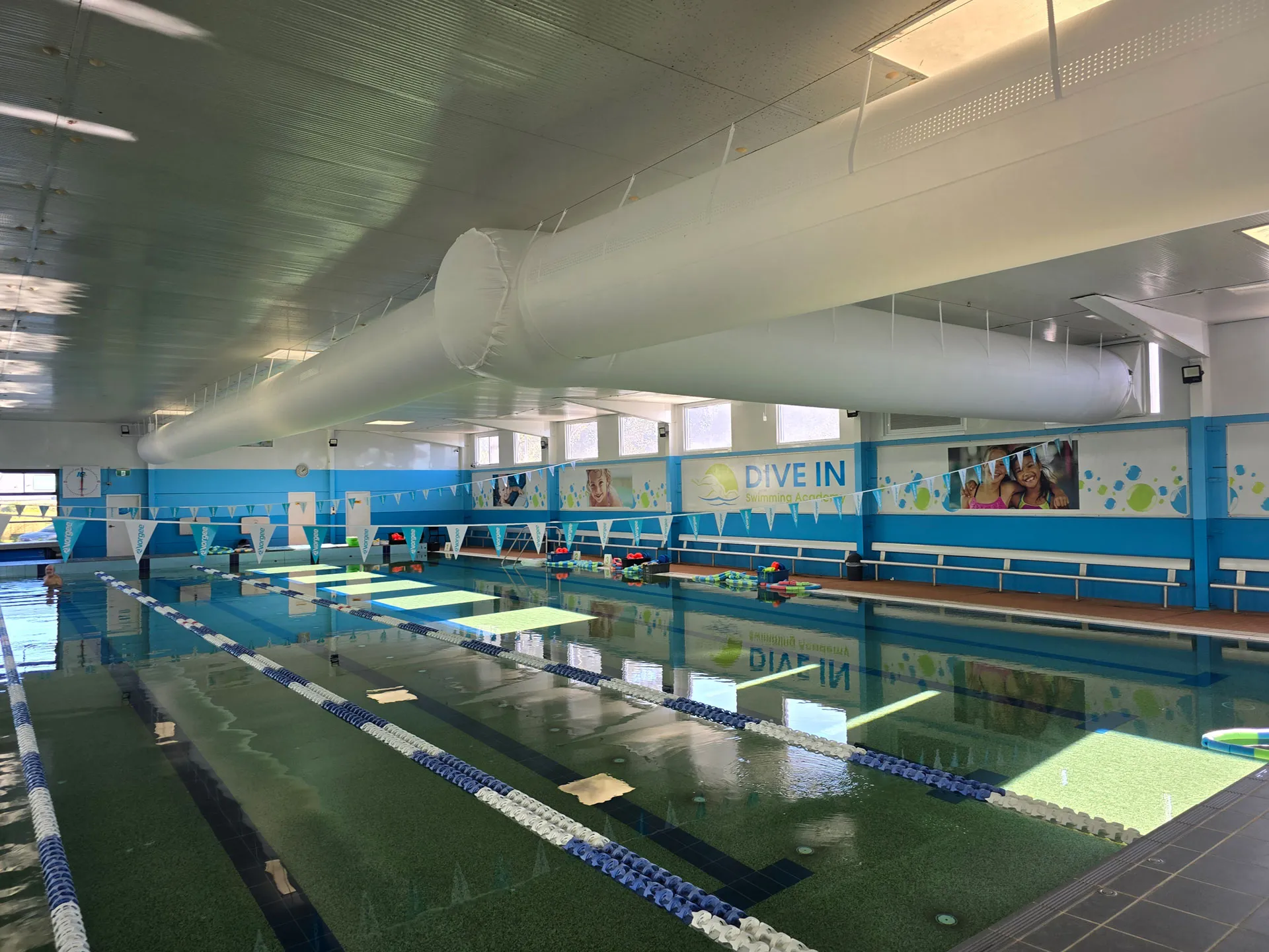 Indoor aquatic centre pool hall with a white fabric supply-air duct along the ceiling